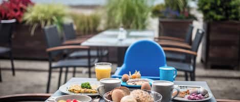 En uteservering med ett bord dukat för frukost, inklusive tallrikar med mat, en skål med frukt och en kaffekopp.