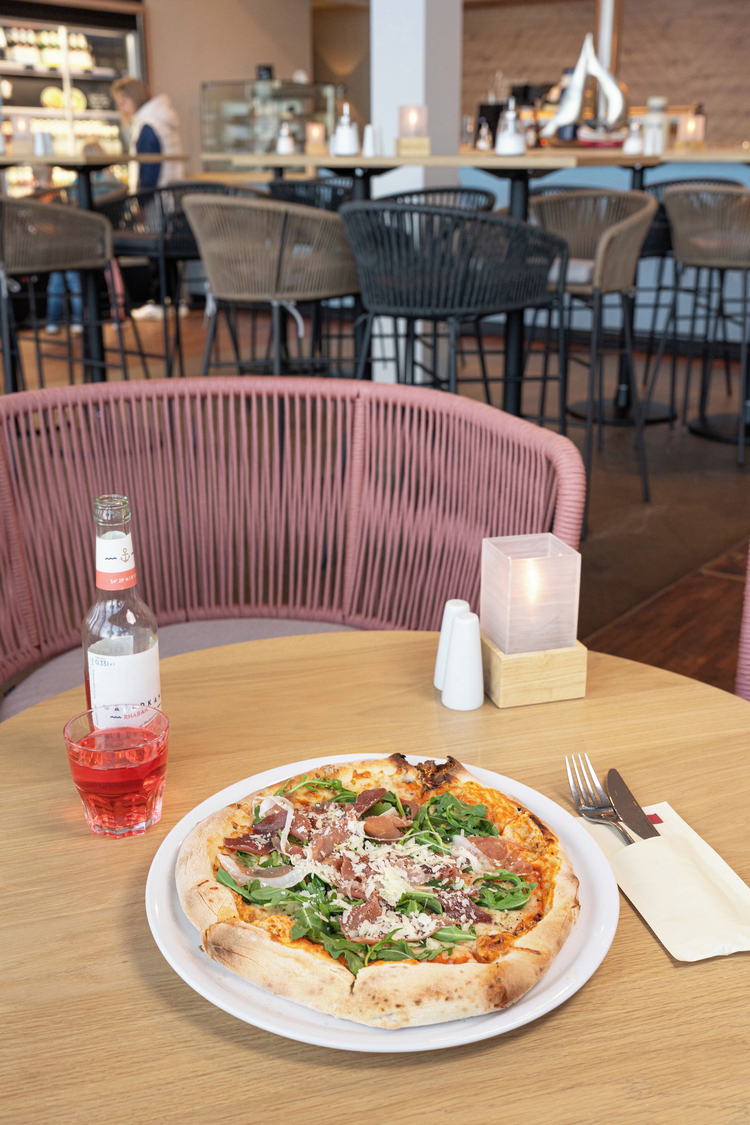 Una mesa de comedor con pizza, una botella y un vaso de bebida roja en un restaurante.