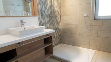 A modern bathroom with a white sink, wooden vanity, a shower with a glass door, and a mirror above the sink.