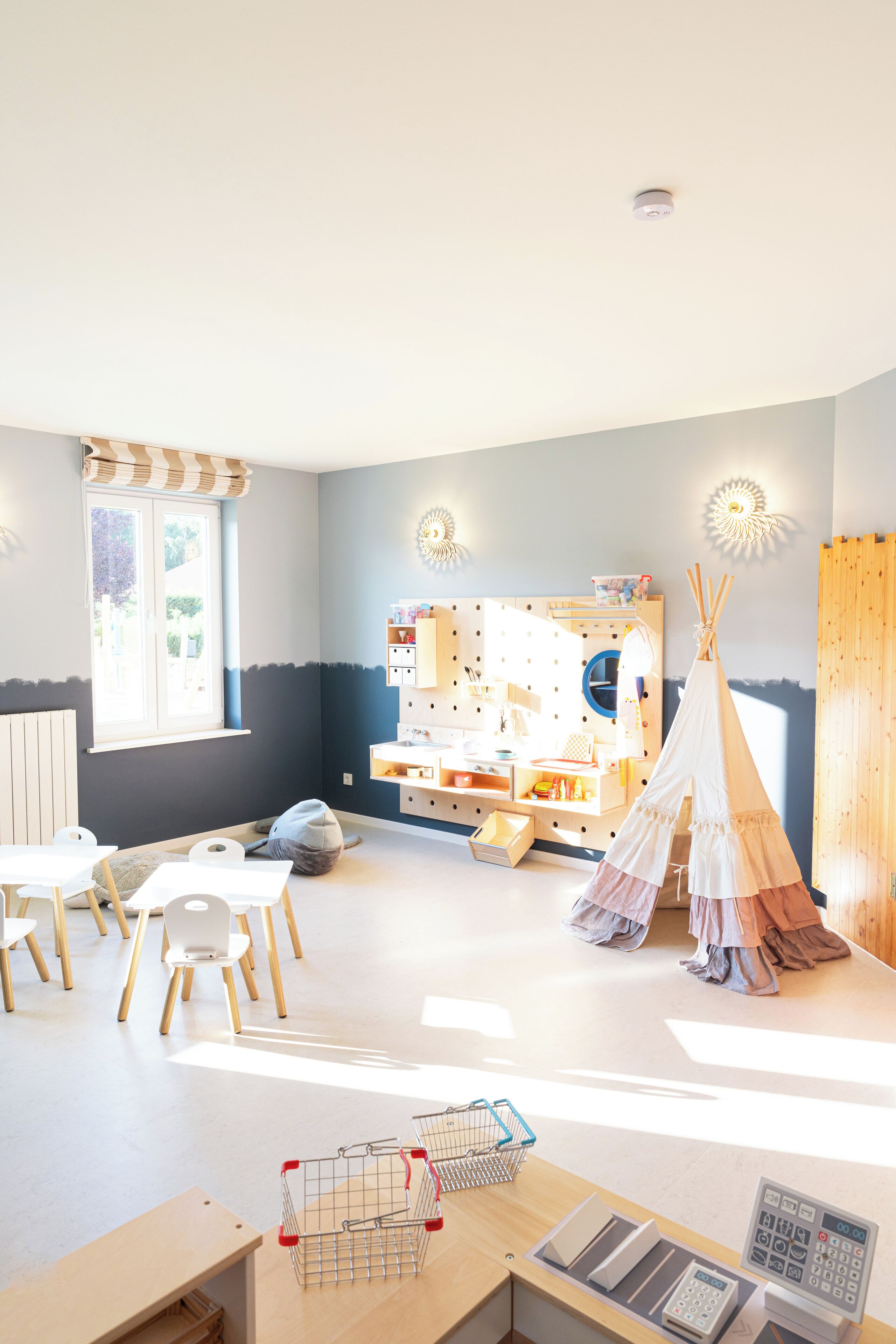 A bright, well-lit room with a window, a play area with a white teepee, and a wooden playhouse.