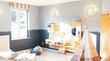 Una habitación luminosa y bien iluminada con una ventana, un área de juegos con una tienda tipi blanca y una casita de madera.