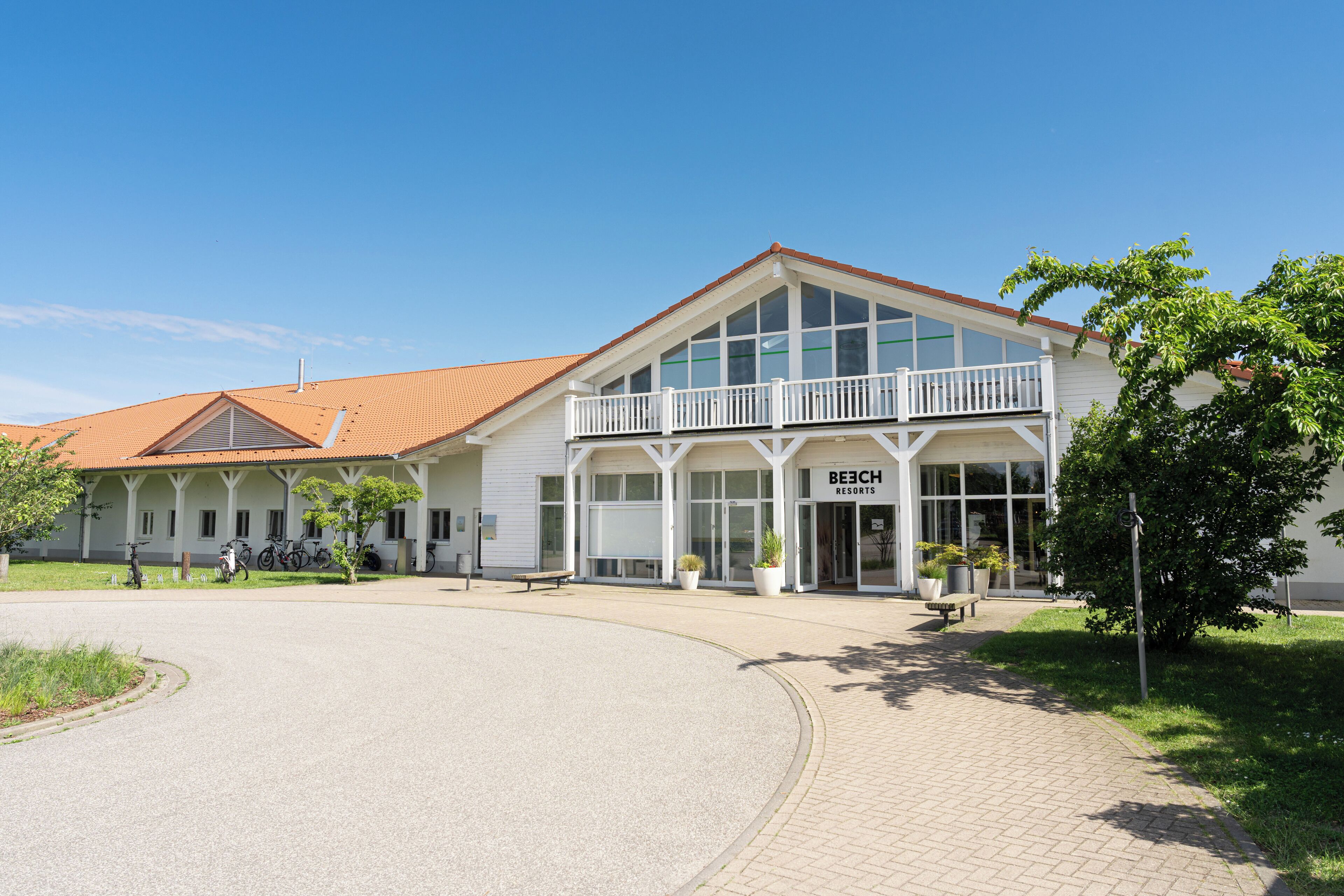 A two-story building with a balcony, a sign reading "Beach Resorts," and a paved driveway.