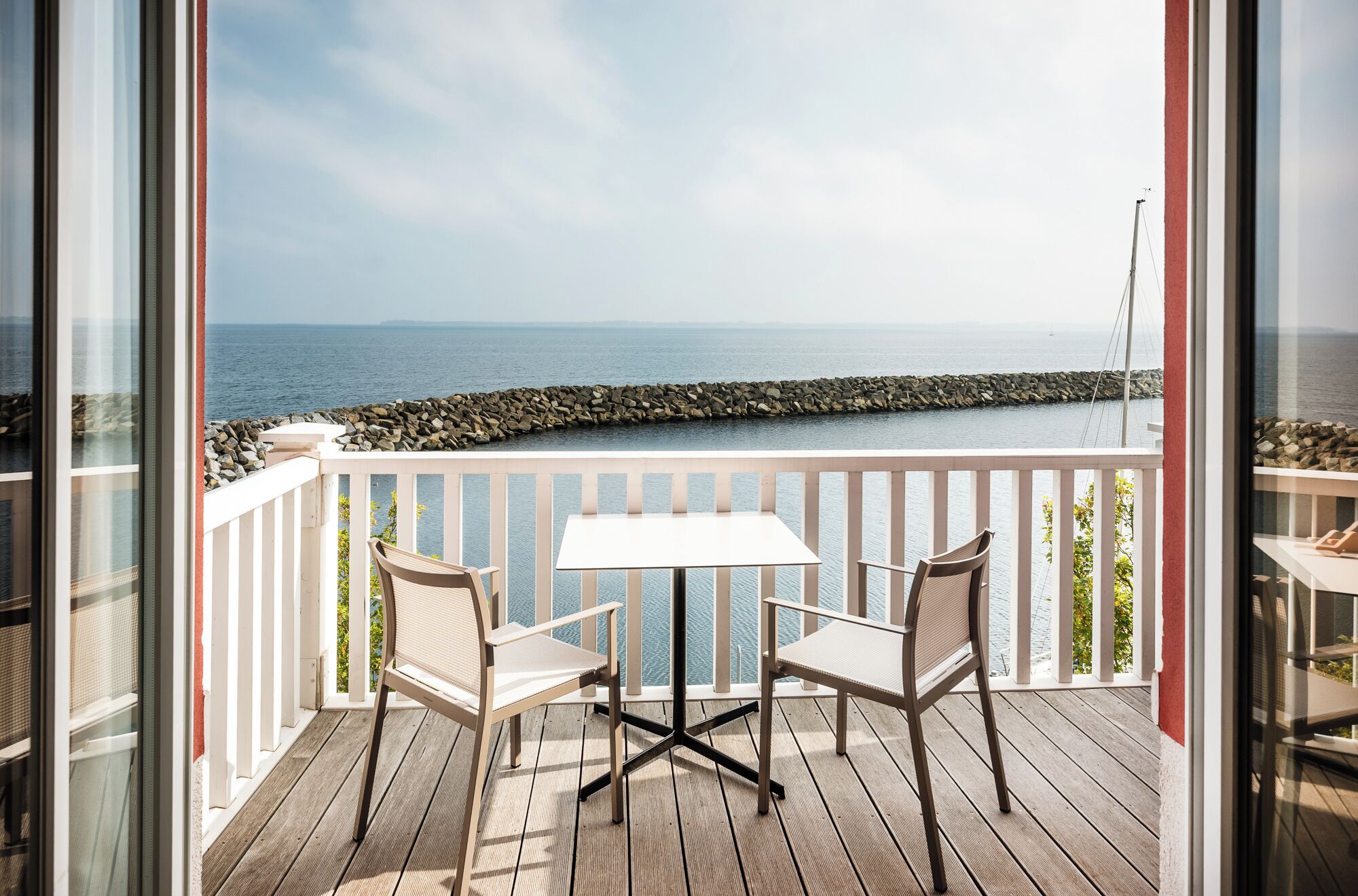 A balcony with a table and two chairs, overlooking a rocky shoreline and the sea.