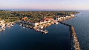An aerial view of a coastal town with a marina, waterfront buildings, and a forested background.