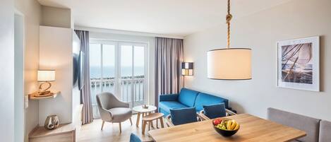 Et moderne hotelværelse med et træspisebord, en blå sofa og en balkon med havudsigt.
