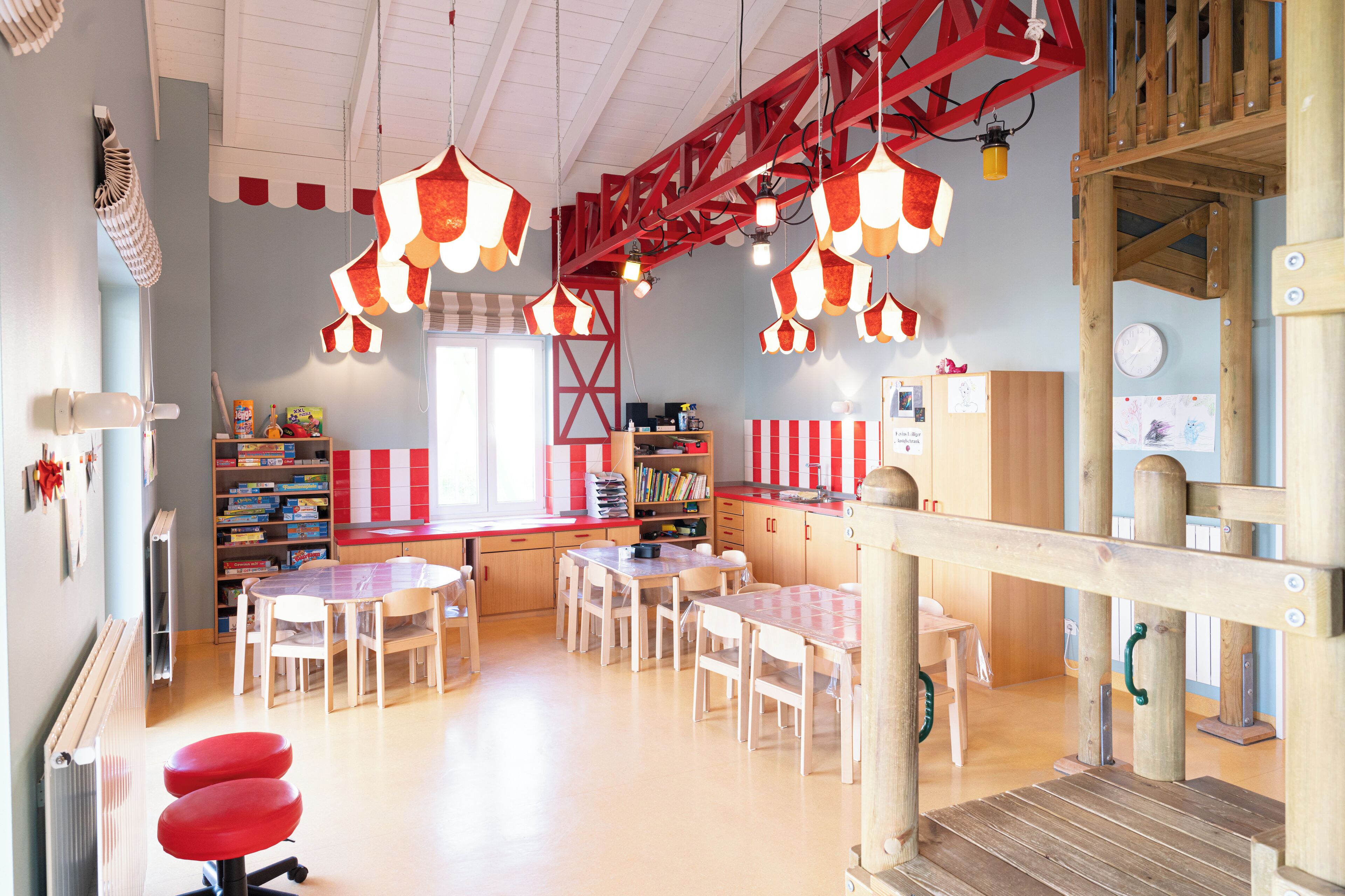 A children's playroom with tables, chairs, and a wooden play structure.