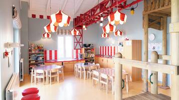 Ein Kinderraum mit Tischen, Stühlen und einer Holzspielanlage.
