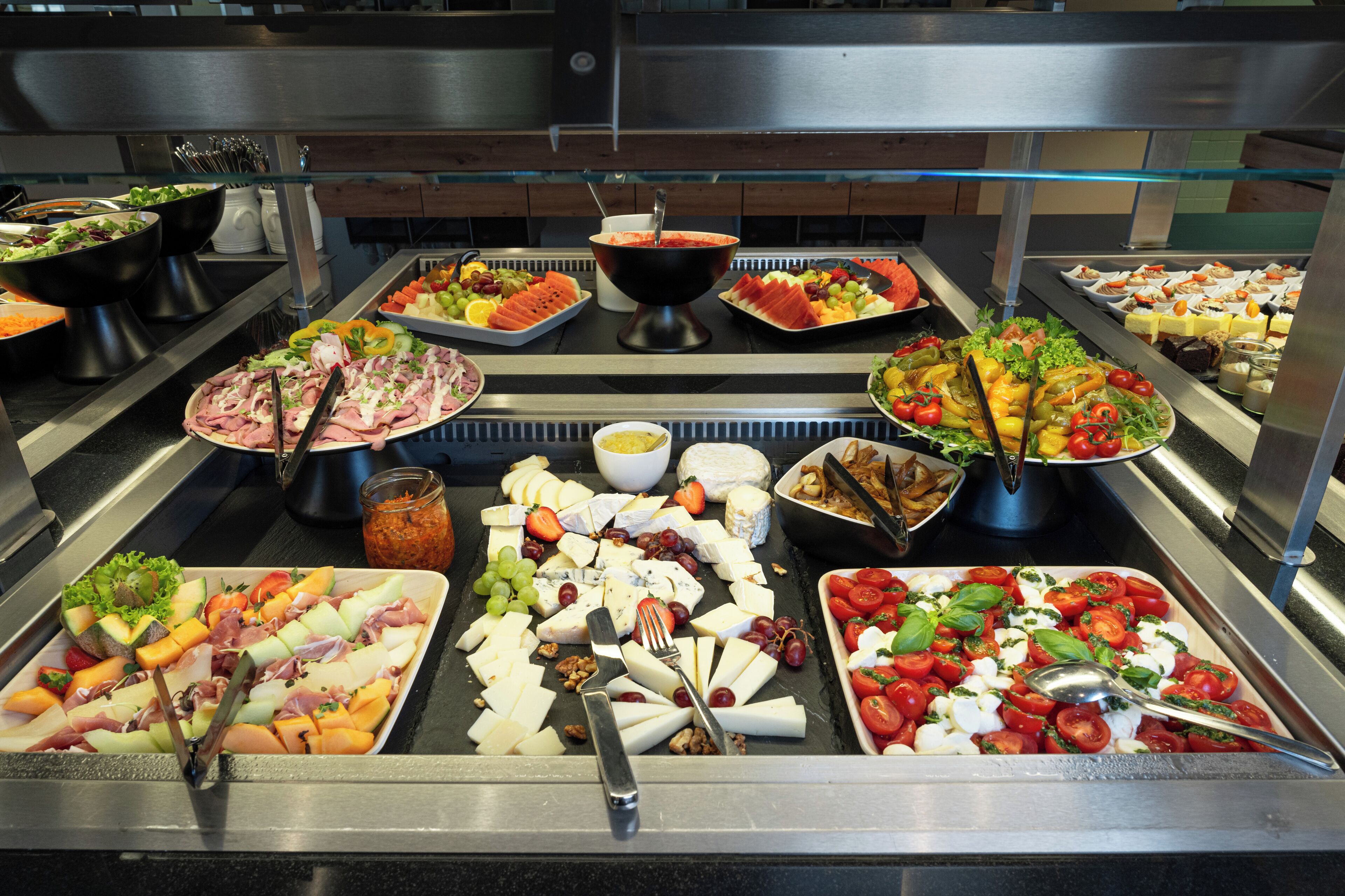 A buffet with various food options including meats, cheeses, fruits, and vegetables.