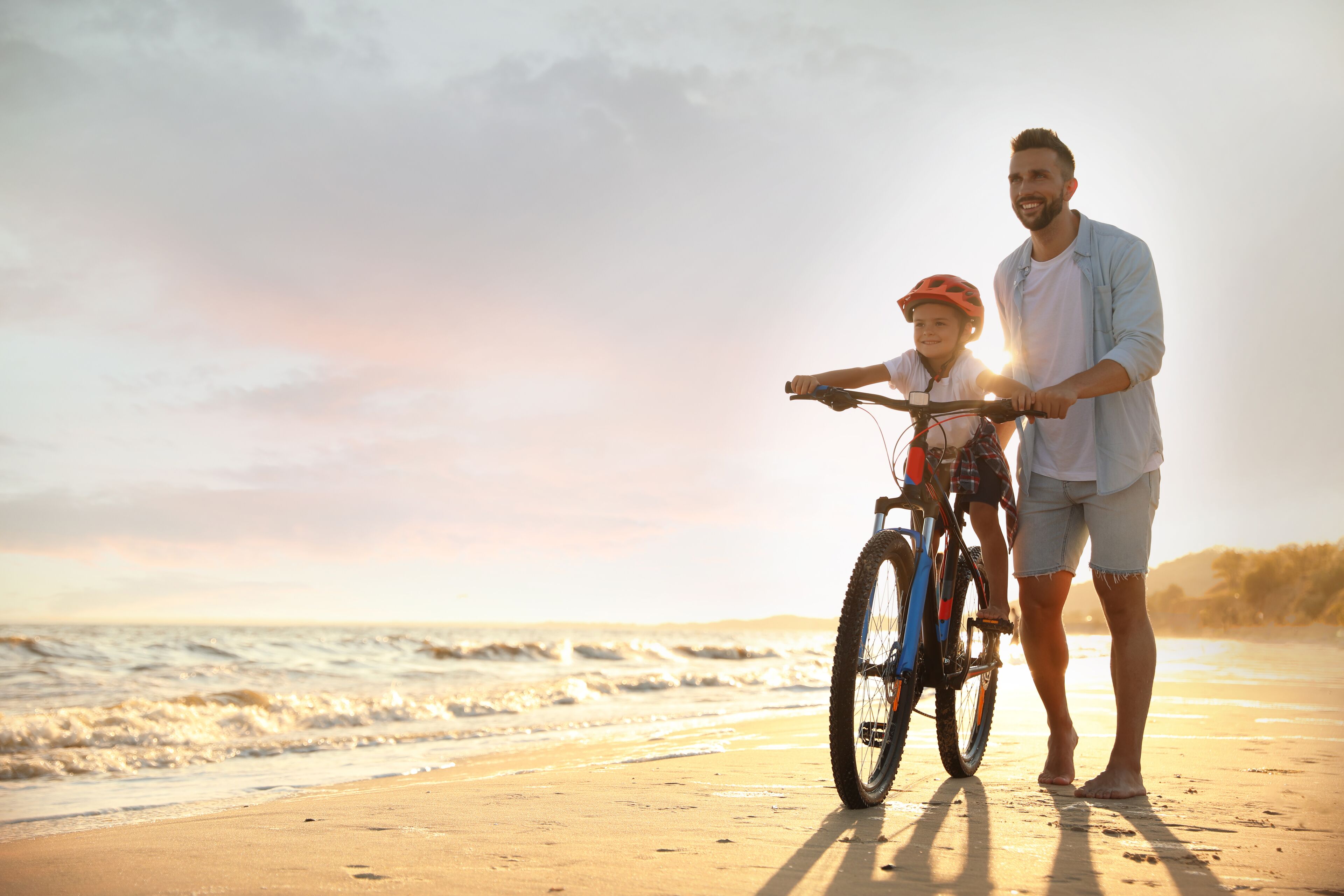 Une scène de plage où l’on voit une personne et un enfant debout à côté d’un vélo.