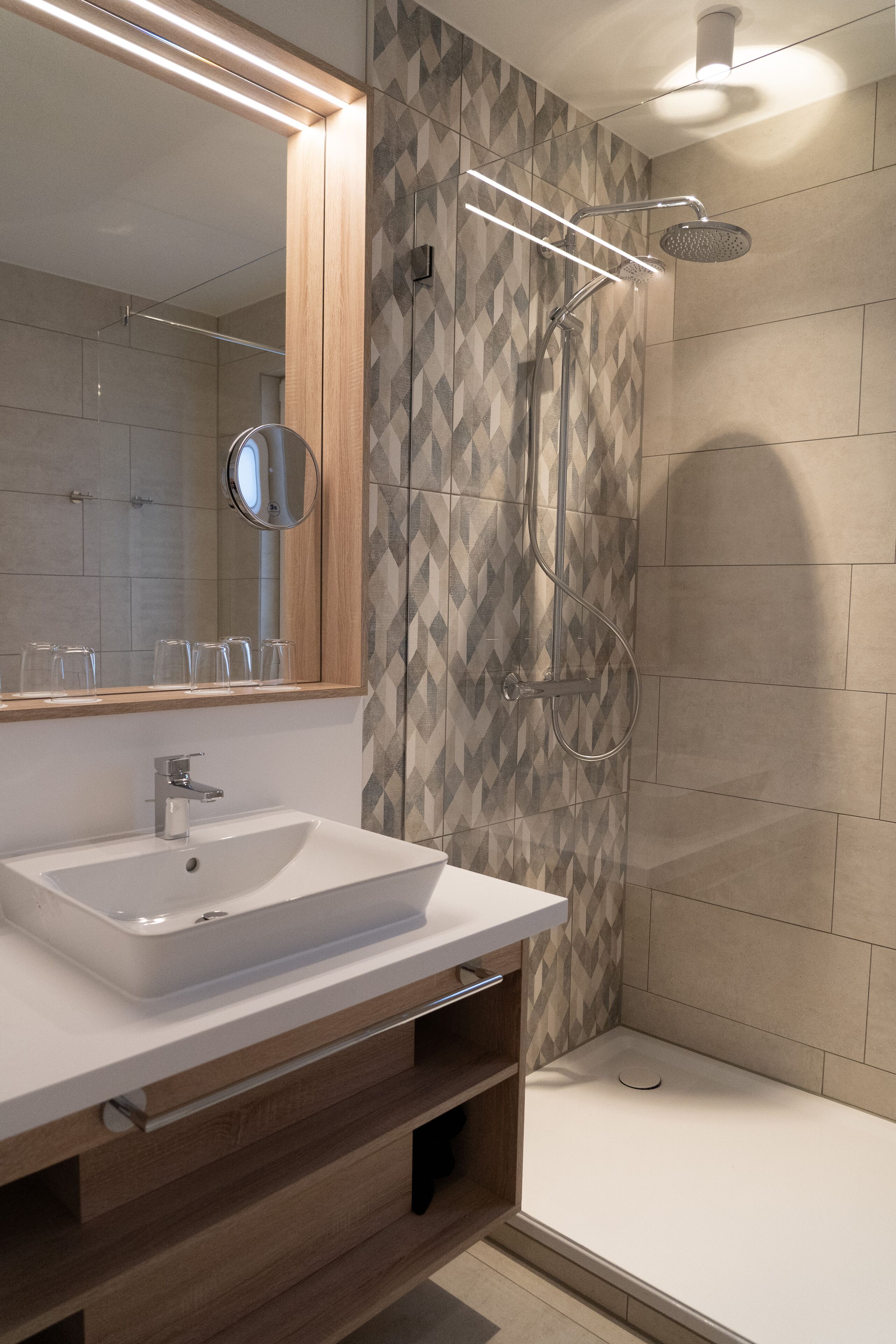 Een moderne badkamer met een grote spiegel, een witte wastafel en een douche met een handdouche.
