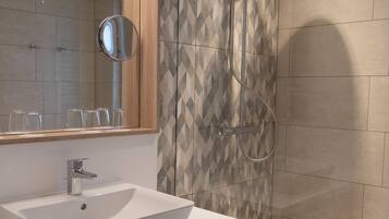 Een moderne badkamer met een grote spiegel, een witte wastafel en een douche met een handdouche.