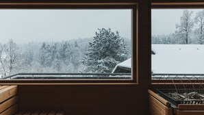 Een kamer met een groot raam dat uitkijkt over een besneeerd landschap met bomen en een heuvel.