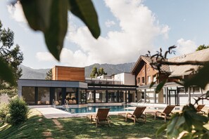 Un área de piscina moderna al aire libre con sillones de descanso, cielo despejado y montañas al fondo.