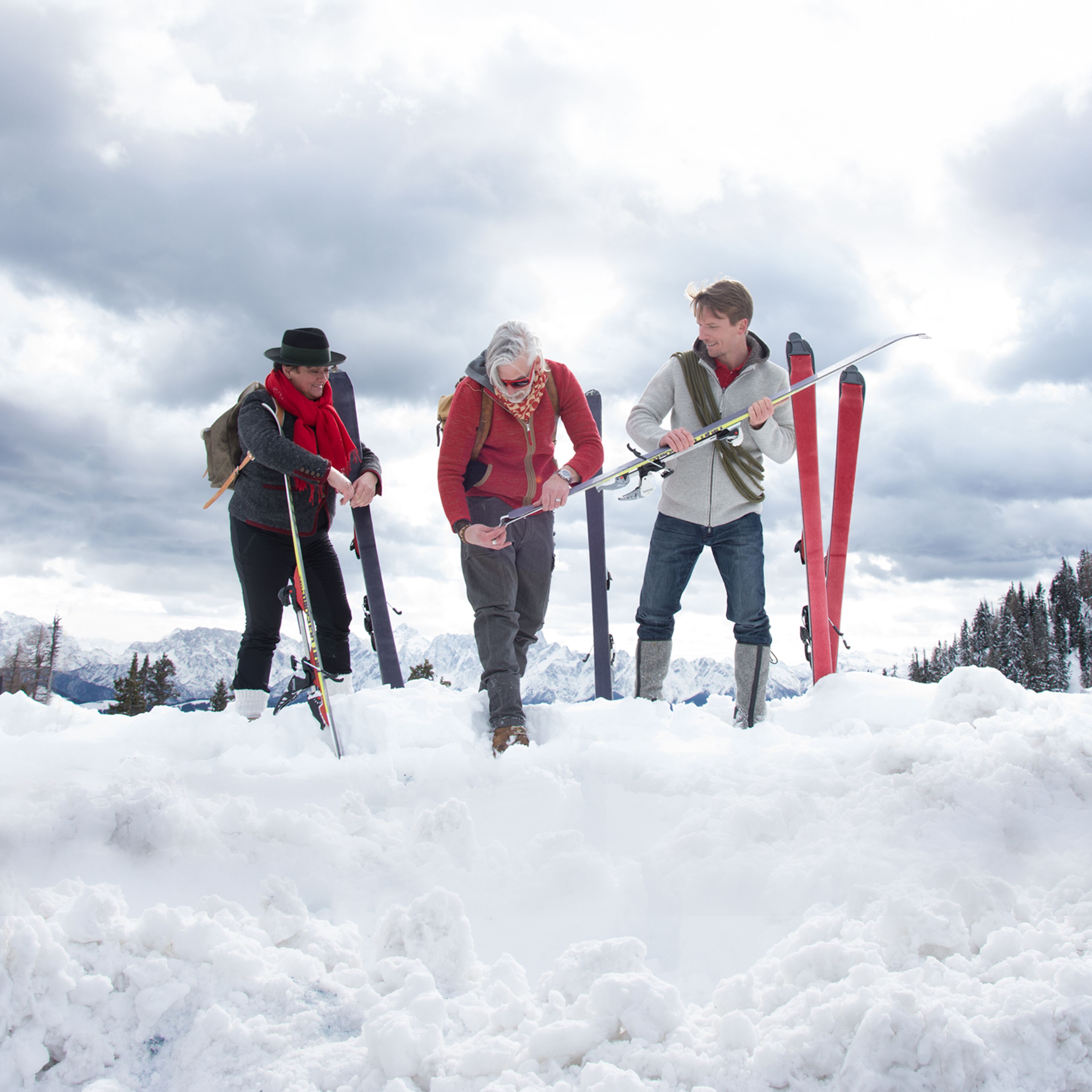 Three people in a snowy landscape with mountains in the background.