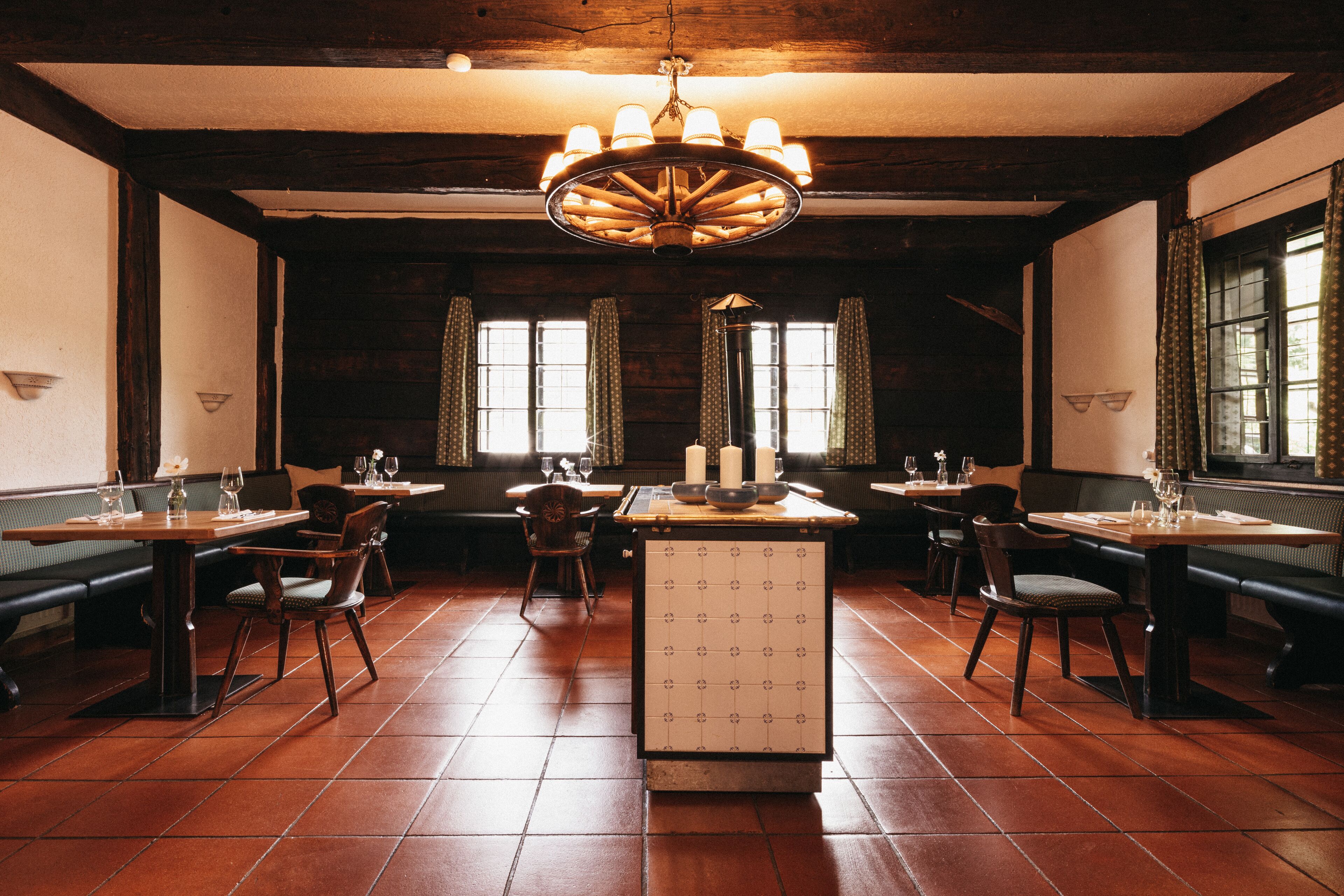 A restaurant with wooden tables, chairs, and a central island with a tiled front.