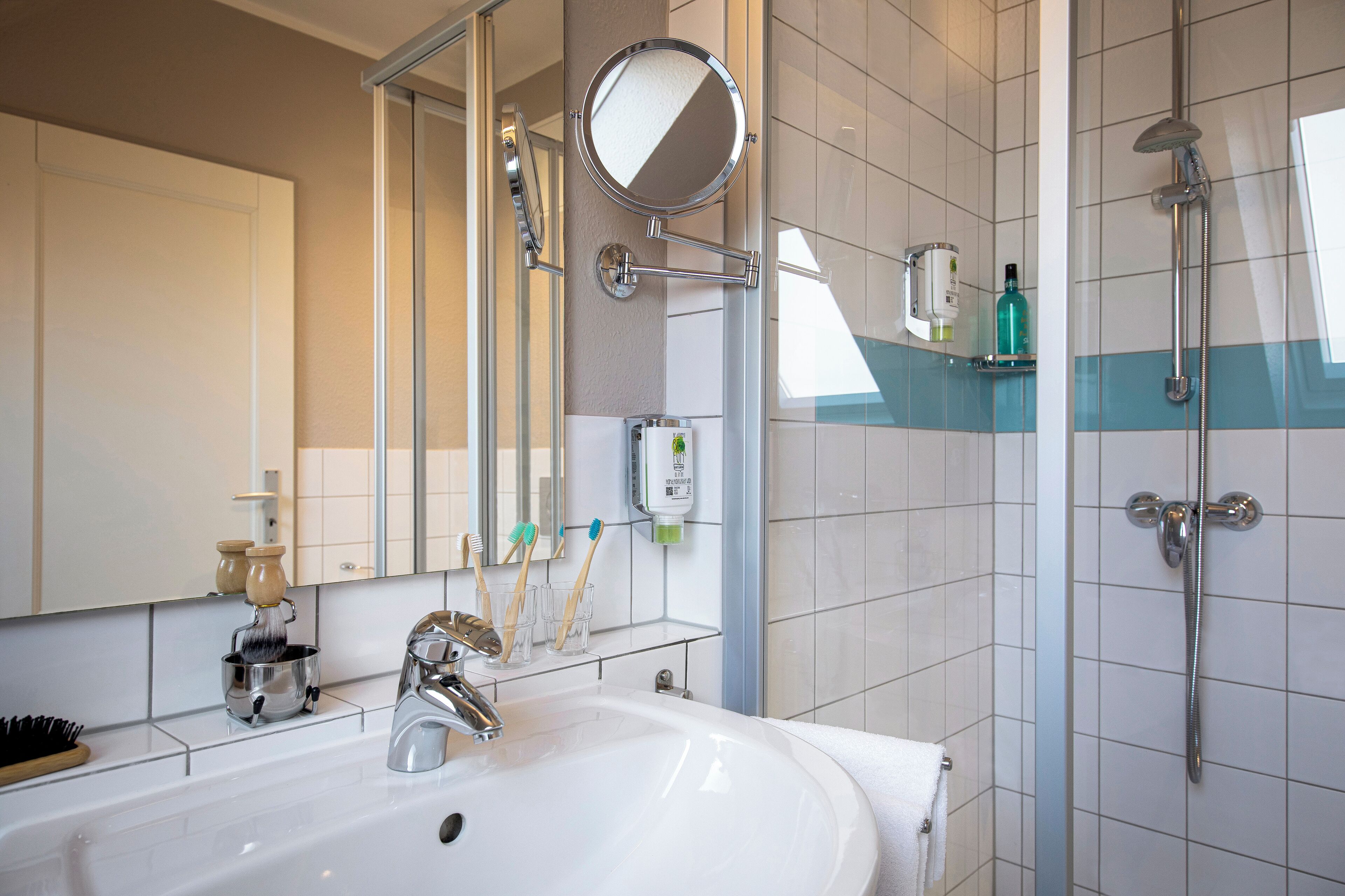 Un baño con lavamanos, espejo, porta cepillos de dientes y ducha.