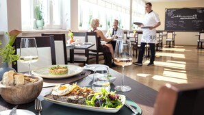 A restaurant with a dining table set for two, a waiter, and a chalkboard menu in the background. - TUI BLUE Sylt (Sylt)