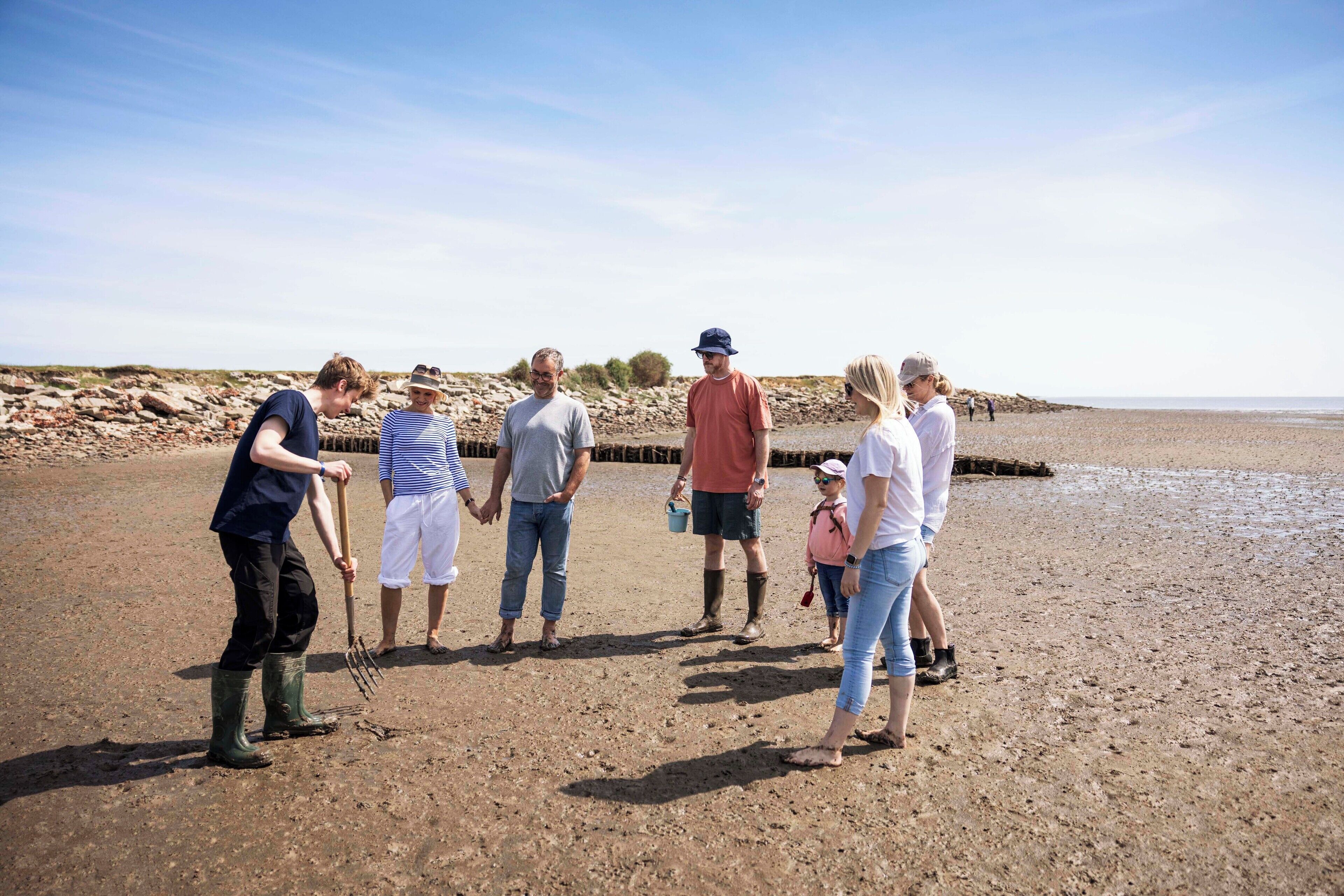 A group of people on a sandy beach with a rocky shoreline in the background.