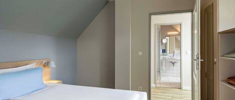 Un dormitorio con cama, lámpara de noche y vista al baño.