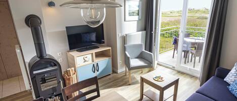Uma sala de estar moderna com uma lareira a lenha, uma televisão, uma mesa de jantar com cadeiras e uma varanda com mobiliário de exterior.