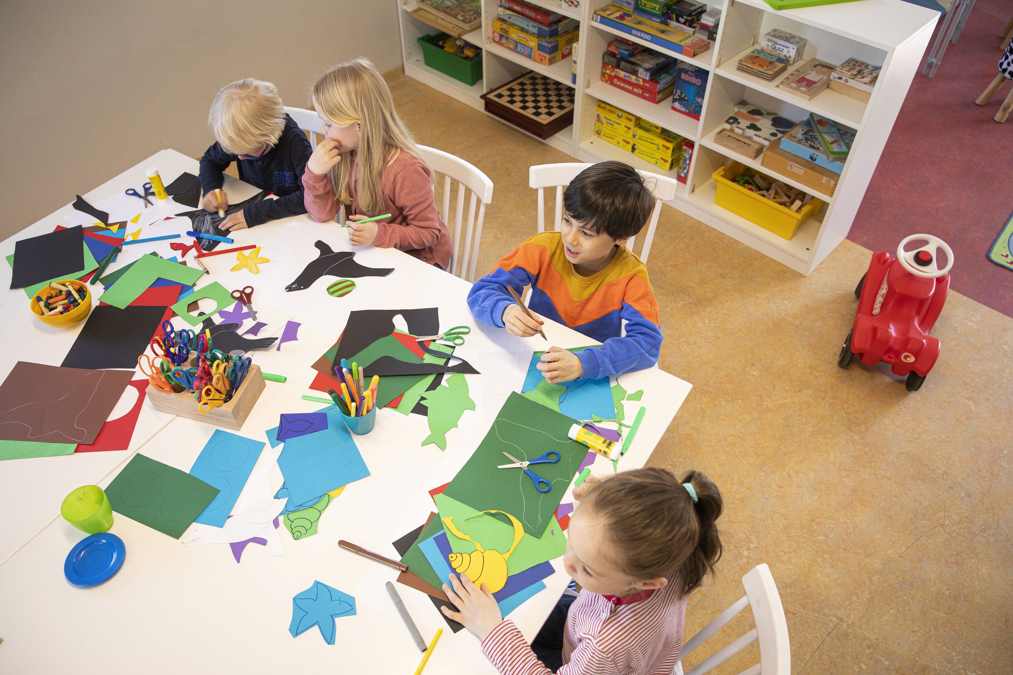 A classroom with children engaged in a craft activity, surrounded by various art supplies and educational materials.