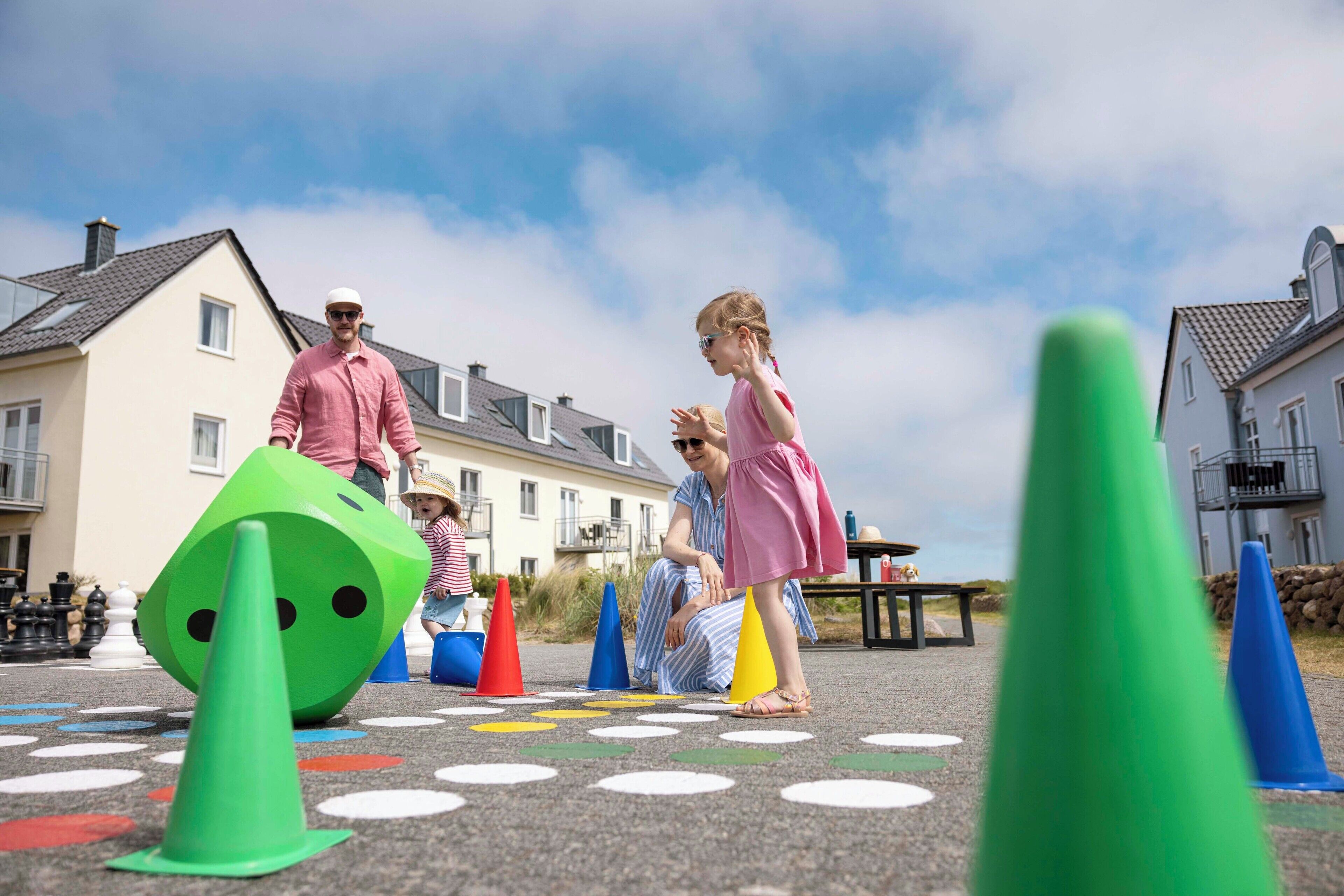 Niños jugando con conos de colores y un dado verde sobre un pavimento estampado.