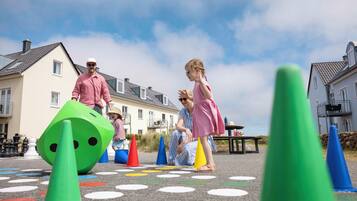 Children playing with colorful cones and a green dice on a patterned pavement.