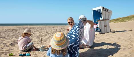 Escena de playa con una silla de playa identificada con el número 5069, un niño jugando con un juguete y una mujer con un vestido blanco.