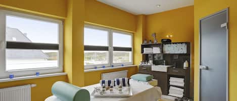 A room with two beds, a window, a radiator, a shelf with toiletries, and a door.