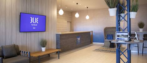 A reception area with a wooden reception desk, a blue sign, a bench, and hanging plants.