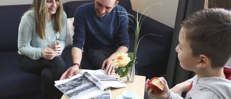 A family sitting on a couch with a magazine, a cup, and a vase with flowers on a table.