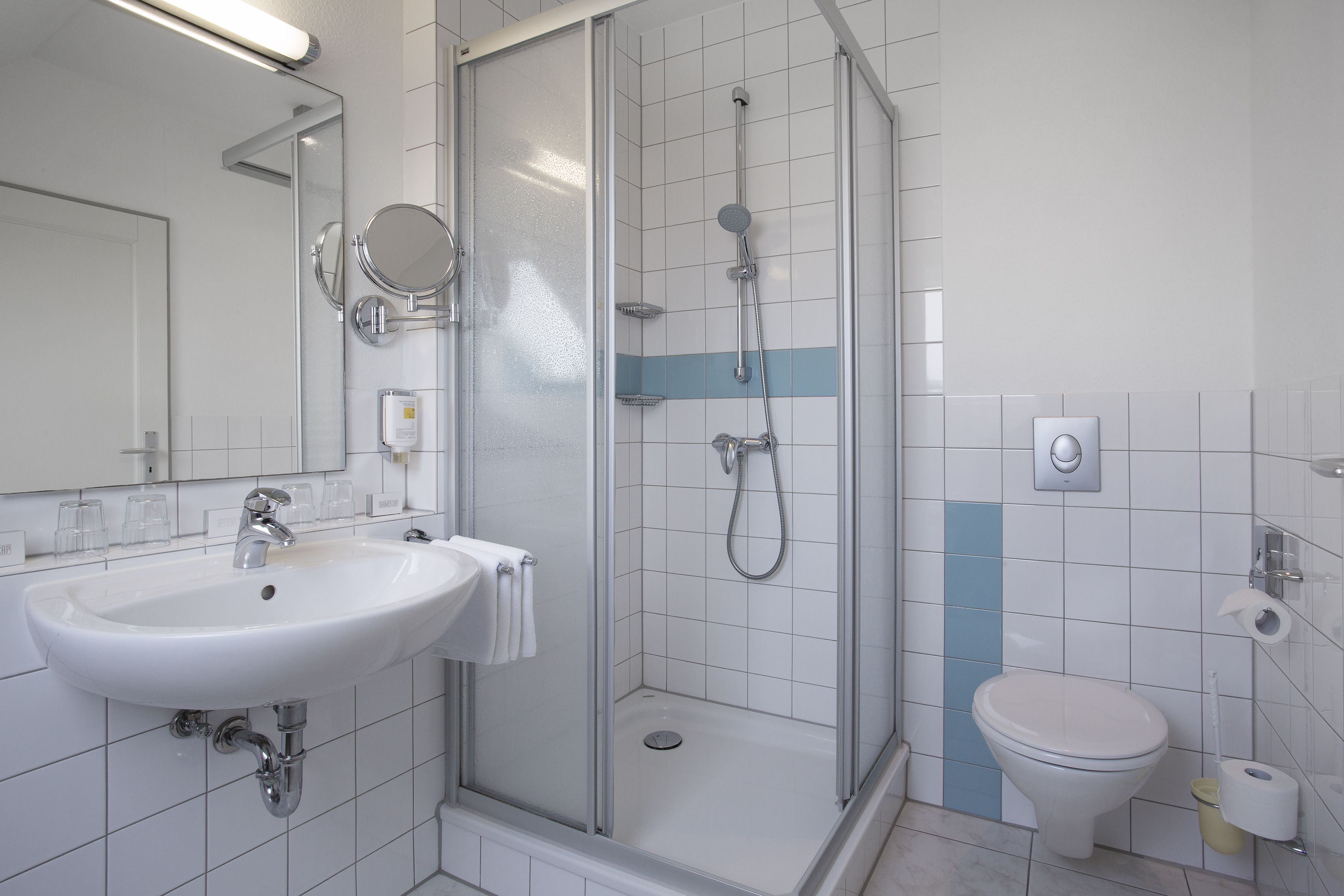 Moderni kylpyhuone, jossa on lasiseinällä varustettu suihku, valkoinen pesuallas ja wc.