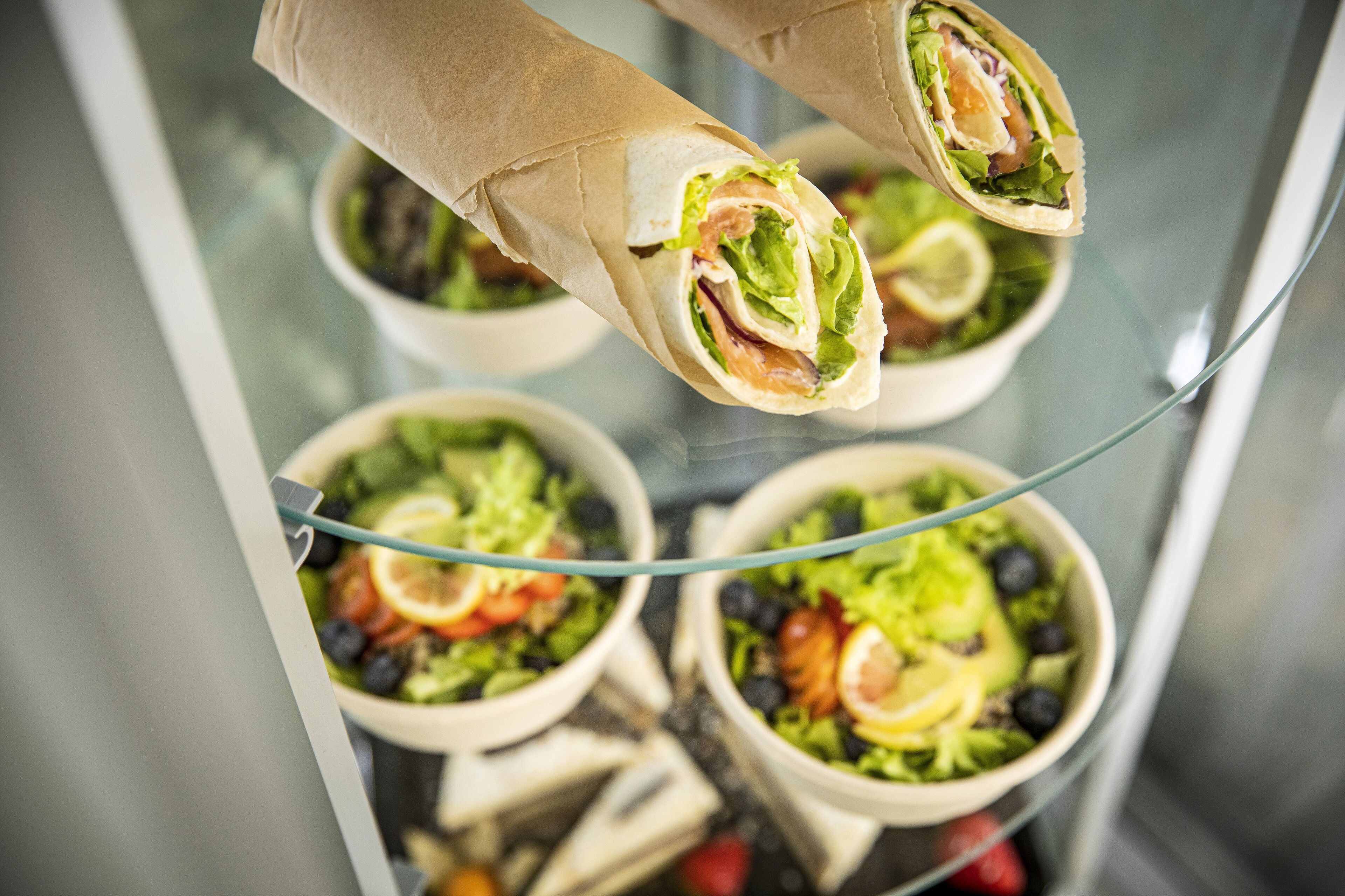 A glass display case with various salads and wraps.