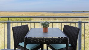 A balcony with a table and two wicker chairs, overlooking a flat landscape with a body of water in the distance. - TUI BLUE Sylt (Sylt)