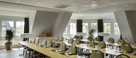 A conference room with long tables, chairs, and a large window providing natural light.