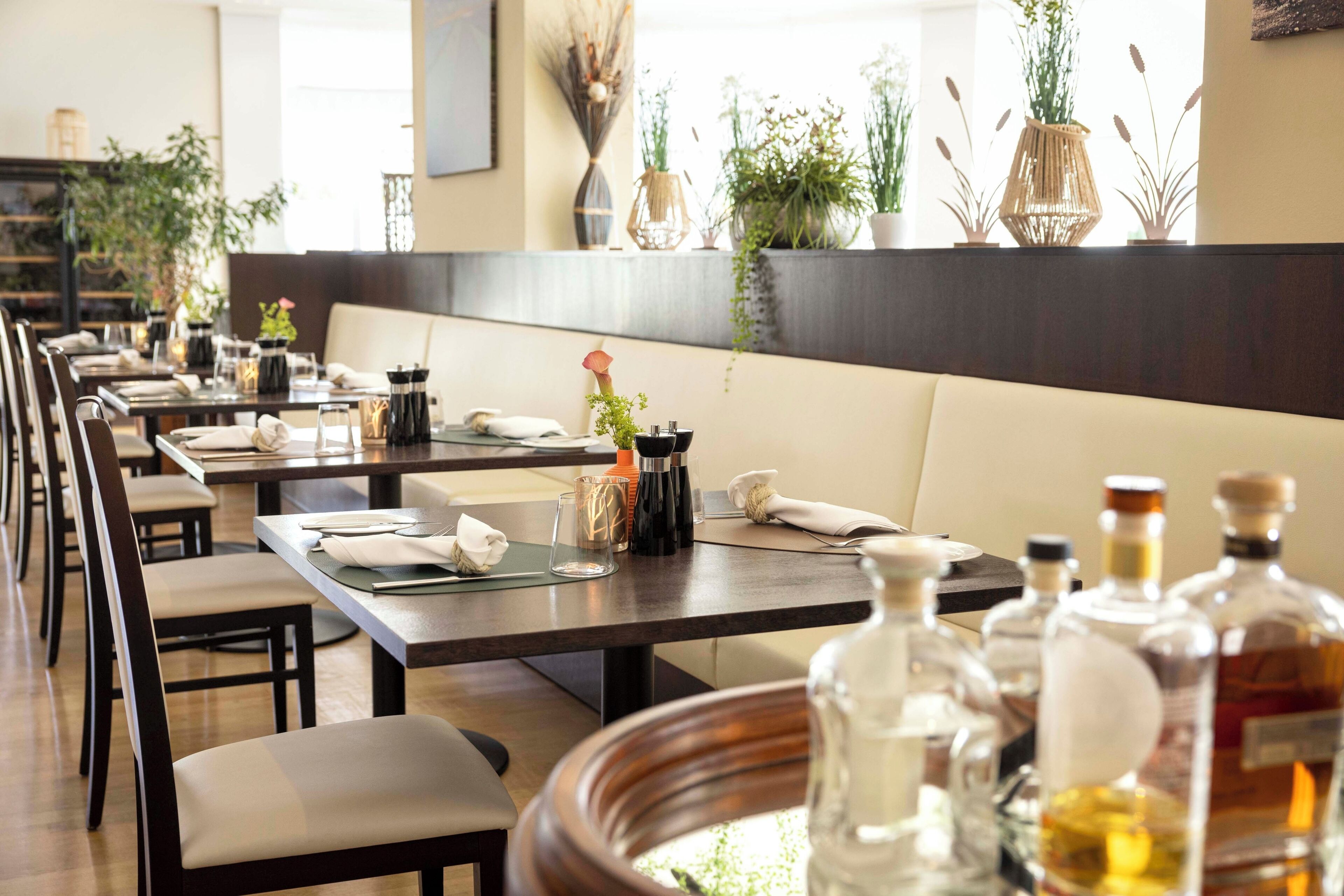 A restaurant with long tables, chairs, and a variety of bottles on the tables.