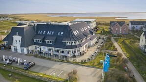 A large building with a curved roof, a parking area, and a view of a body of water. - TUI BLUE Sylt (Sylt)