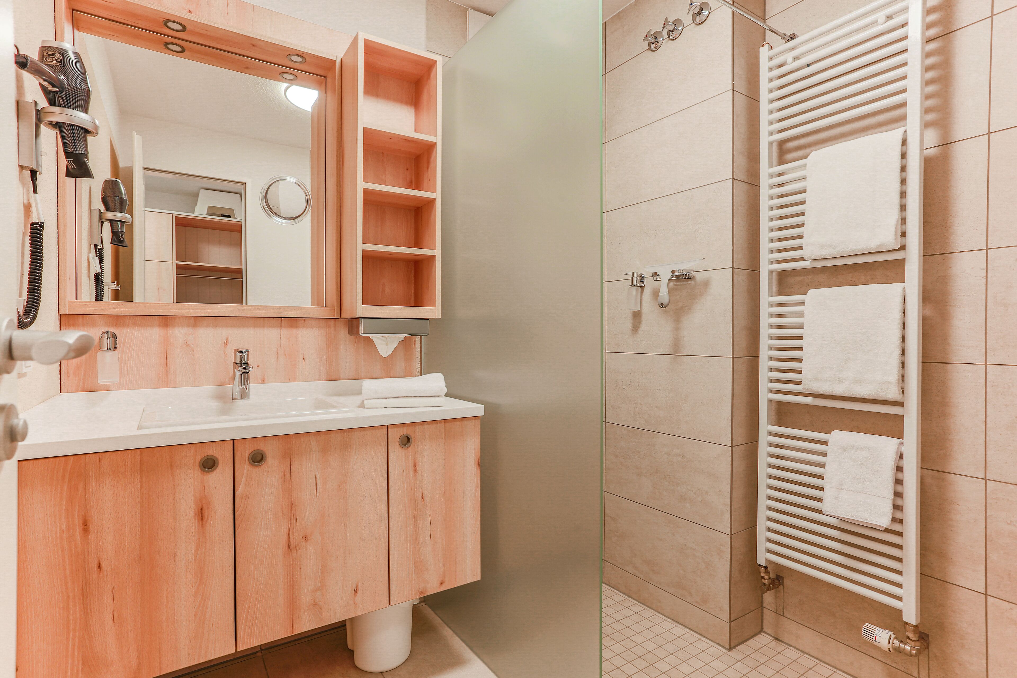 Un baño moderno con tocador de madera, un espejo grande, ducha con puerta de cristal y un perchero para toallas.