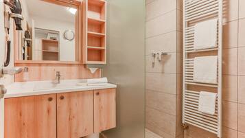 Un baño moderno con tocador de madera, un espejo grande, ducha con puerta de cristal y un perchero para toallas.