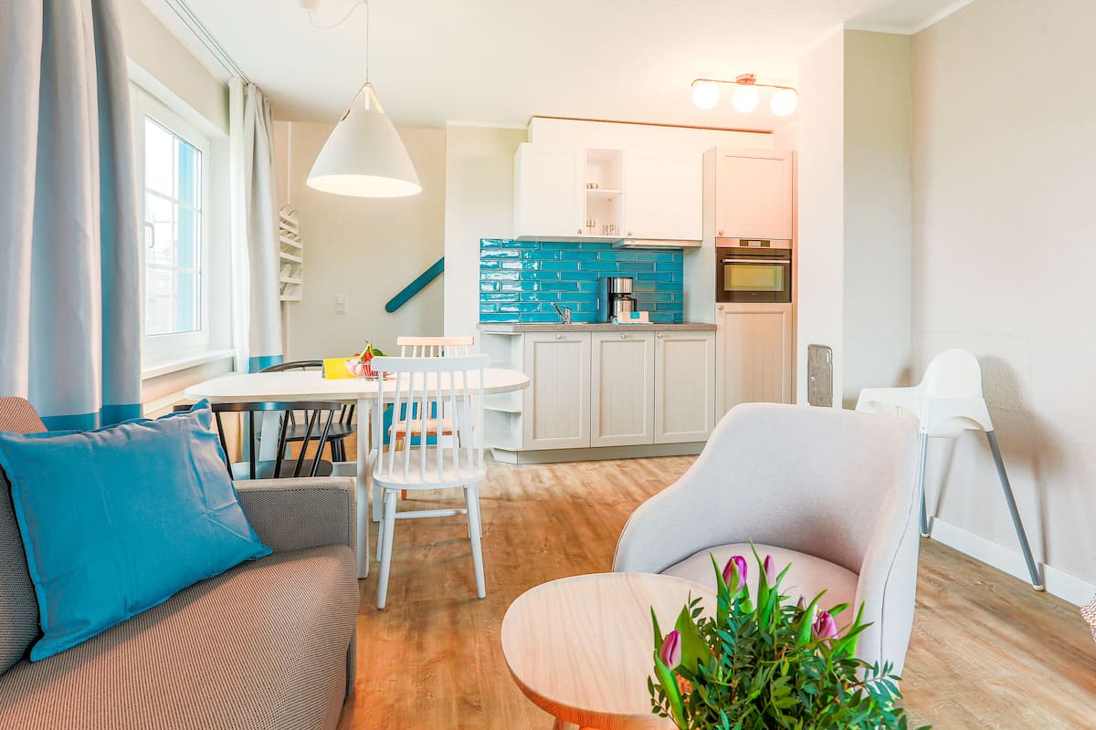 A modern living room with a sofa, a dining table, and a kitchen area with cabinets and a sink.