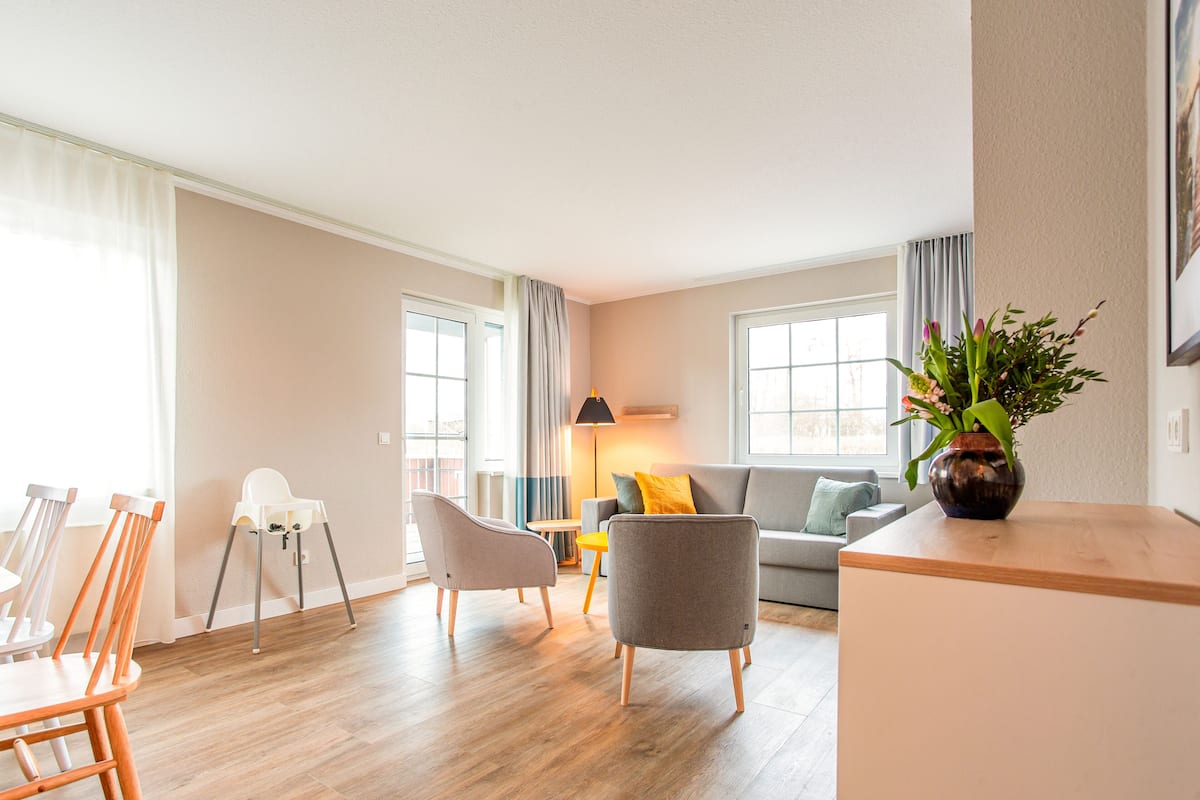 A modern living room with a sofa, chairs, a dining table, and a vase of flowers.