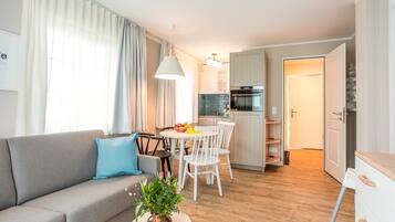 Ein modernes Wohnzimmer mit grauem Sofa, einem Esstisch mit Stühlen, einer Küchenzeile mit Herd und Schränken sowie einer Treppe, die zu einer weiteren Ebene führt.