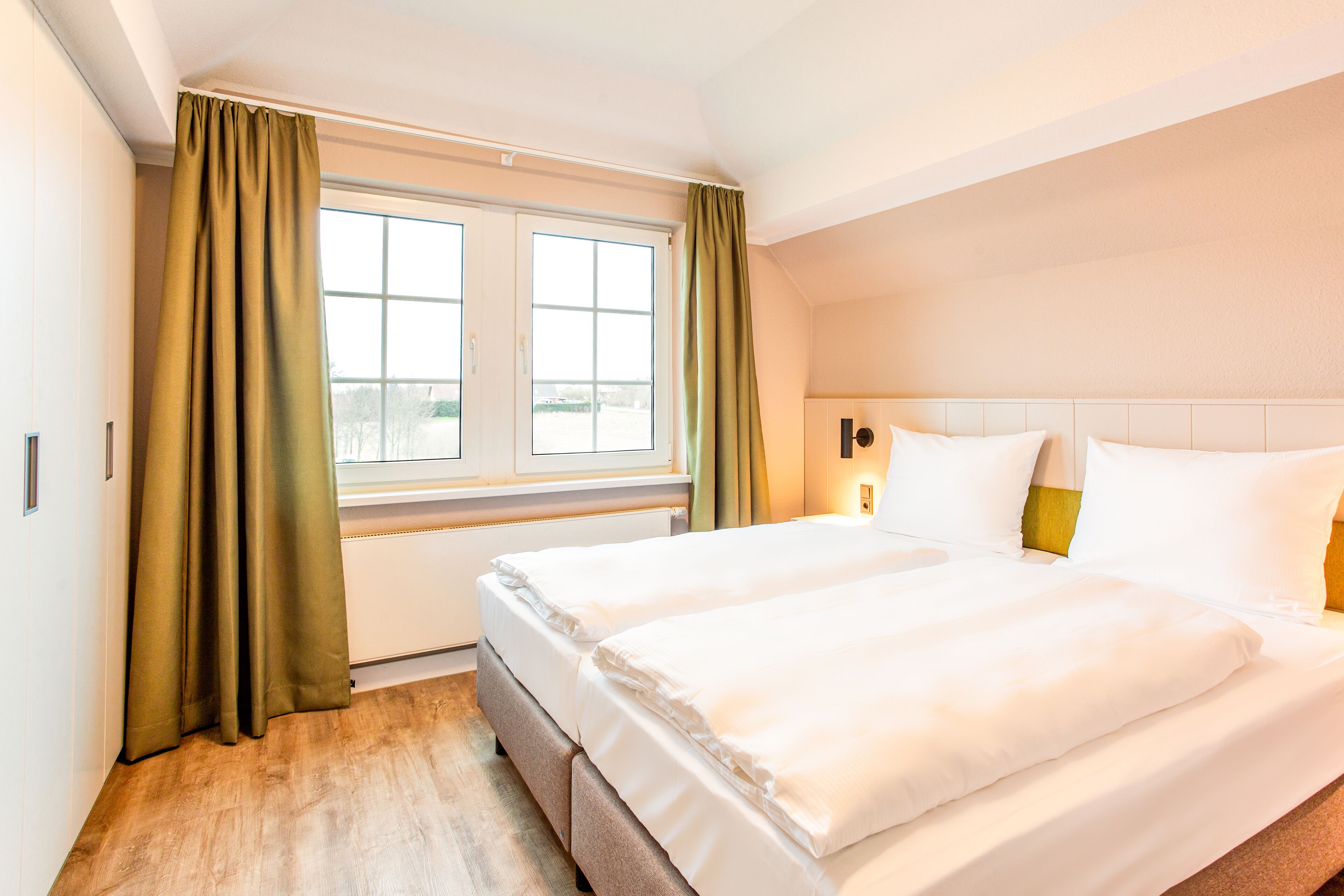 Ein Hotelzimmer mit einem großen Bett, einem Fenster mit Vorhängen und Blick ins Freie.