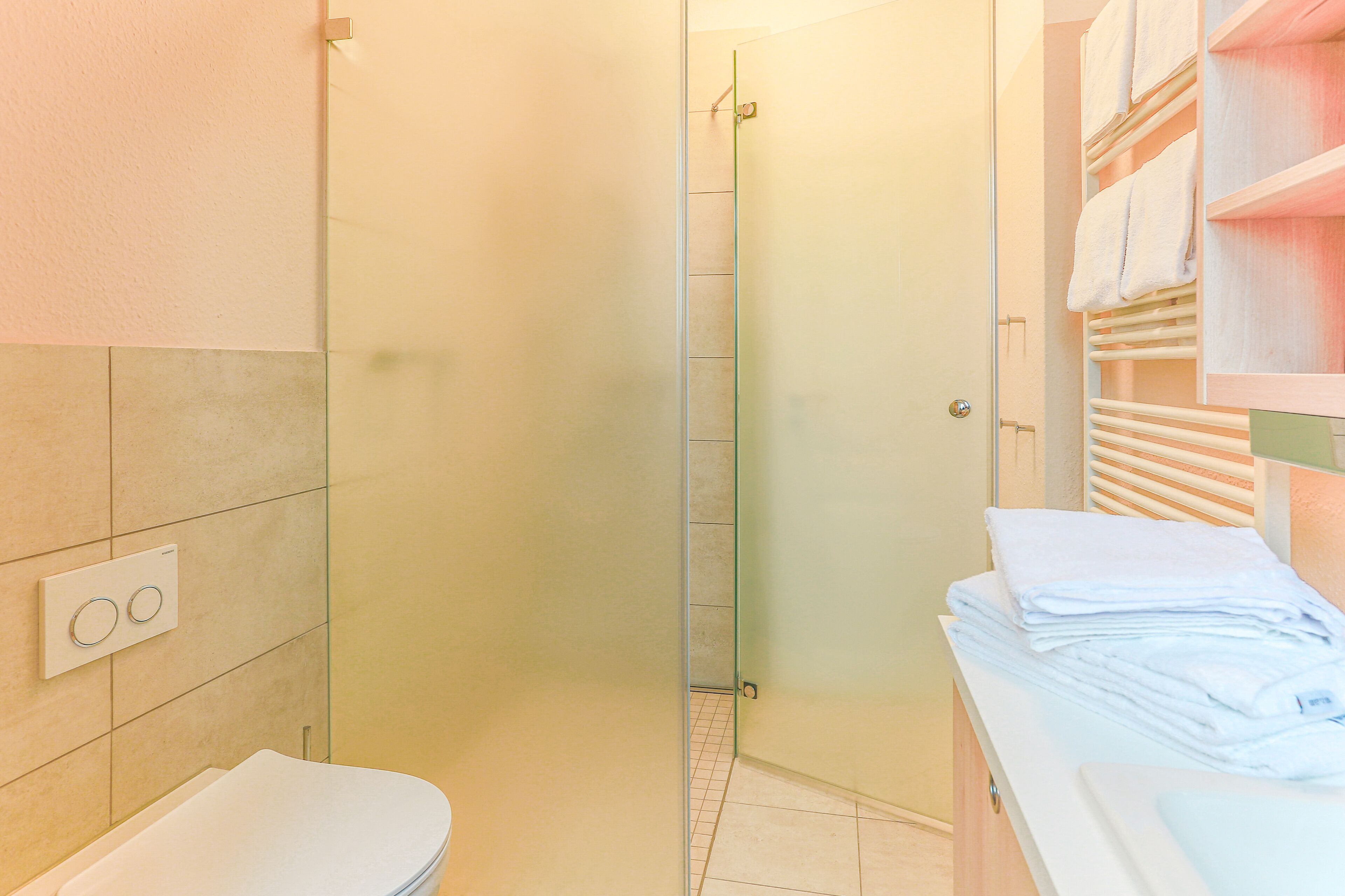 Un baño con inodoro, cabina de ducha de vidrio y toallero con toallas dobladas.