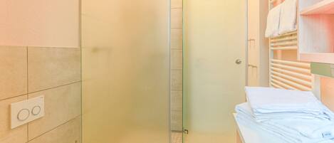 Un baño con inodoro, cabina de ducha de vidrio y toallero con toallas dobladas.