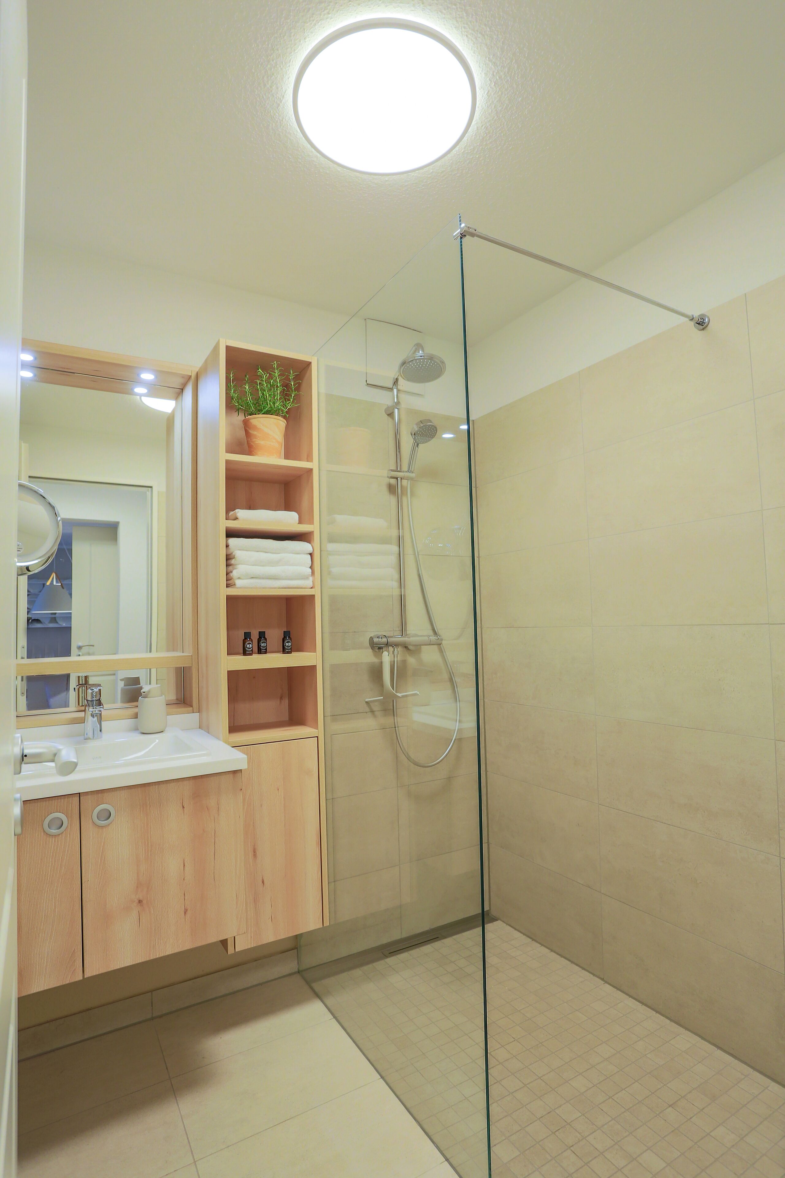Un baño moderno con cabina de ducha de vidrio, tocador de madera y espejo con marco redondo.