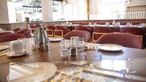 Un comedor con mesas dispuestas para el servicio, incluyendo cubiertos, tazas y saleros y pimenteros.