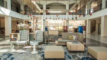 Un hall espacioso con techo alto, una zona de estar central con sofás y sillones, una estantería grande y lámparas decorativas colgantes.
