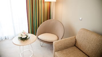 Una habitación con un sofá color beige, un sillón redondo, una mesita con un arreglo floral y una cortina a rayas coloridas.