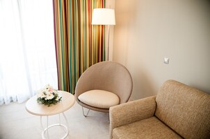Una habitación con un sofá color beige, un sillón redondo, una mesita con un arreglo floral y una cortina a rayas coloridas.
